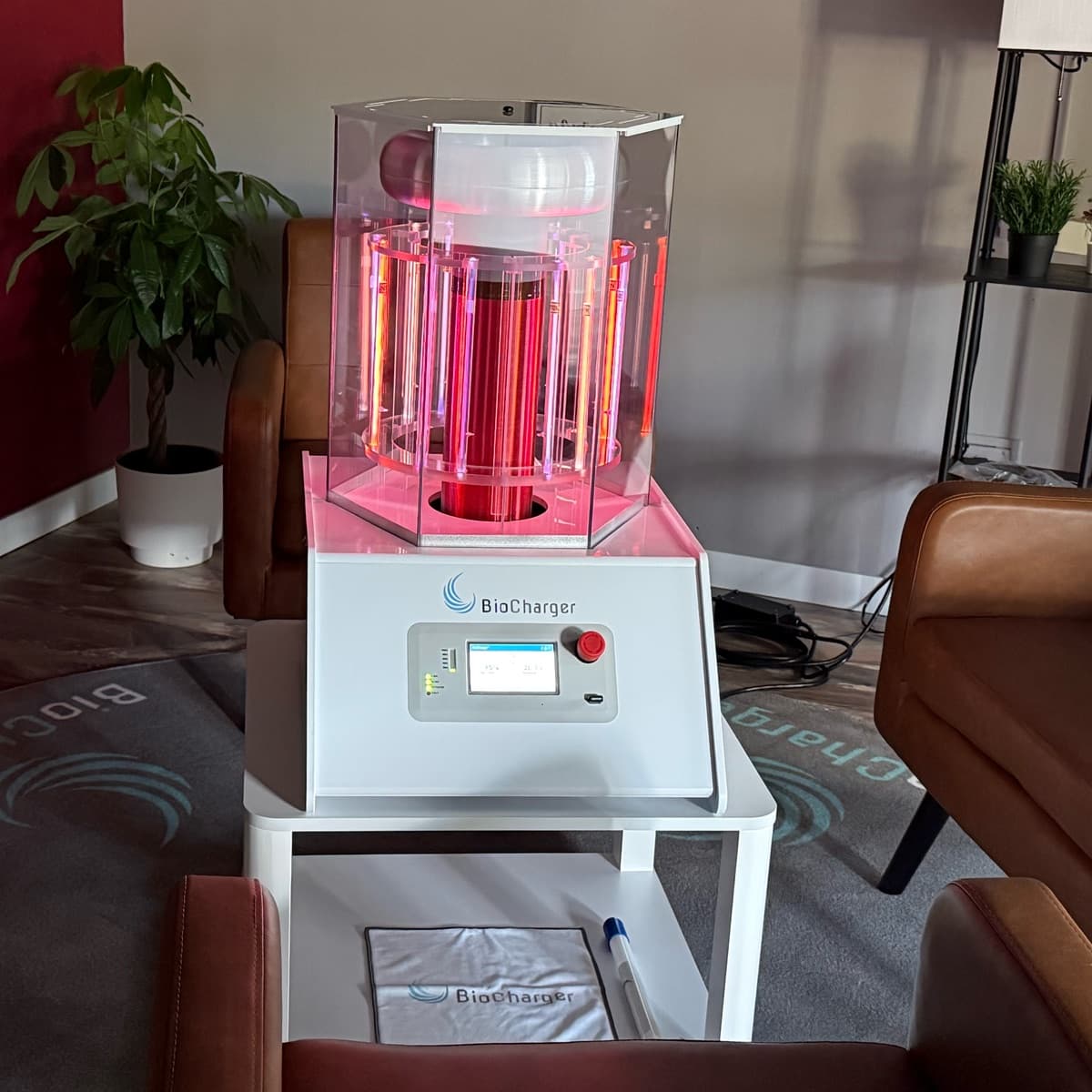 The BioCharger at Elevate Wellness Studio, its coil glowing pink and red inside a clear housing, with leather armchairs around it