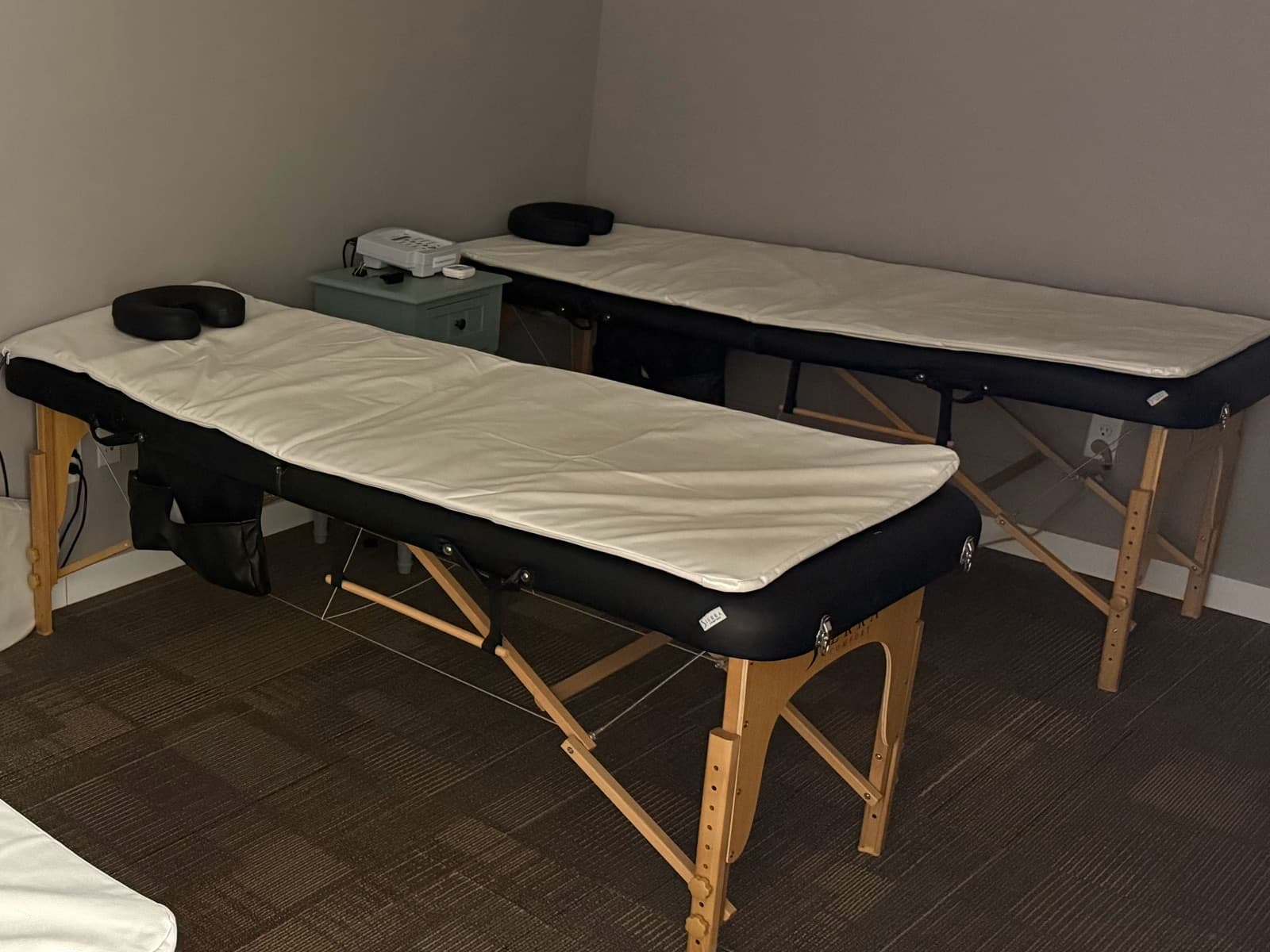 Two treatment tables covered with white full-body PureWave PEMF mats, with a PureWave controller on the nightstand between them