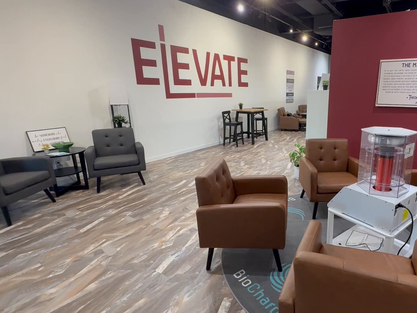 The open lounge at Elevate Wellness Studio: gray armchairs and a bistro table along the white ELEVATE wall, with leather armchairs around the BioCharger in front